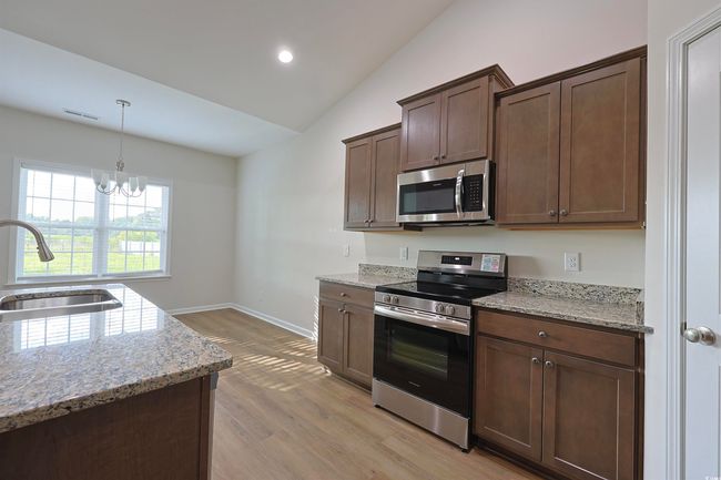 Kitchen featuring stainless steel appliances, vaulted ceiling, light wood-style floors, light stone countertops, and a chandelier | Image 6