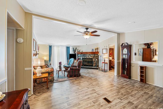 Living room with a textured ceiling, wood finished floors, a ceiling fan, a fireplace, and a decorative wall | Image 13