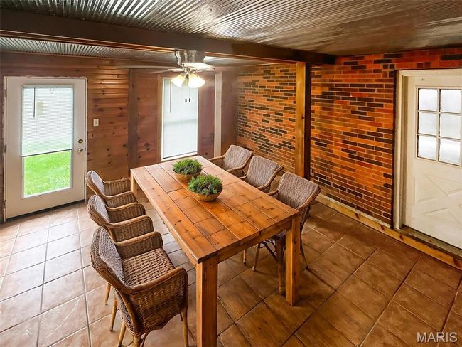Dining area featuring light tile patterned floors, beam ceiling, a ceiling fan, and brick wall | Image 6