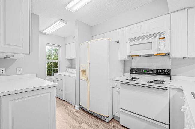 Kitchen featuring white appliances, independent washer and dryer, white cabinetry, and a textured ceiling | Image 9