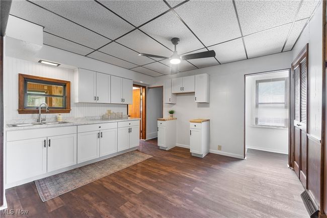 Kitchen with ceiling fan, dark wood finished floors, white cabinetry, and a drop ceiling | Image 8