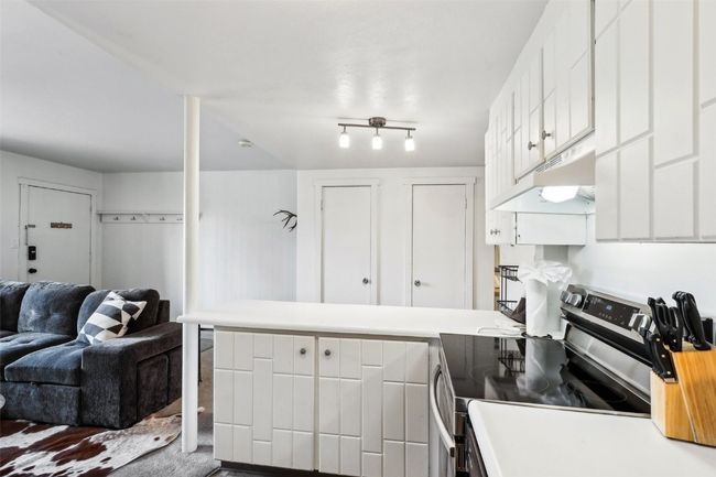 Kitchen with electric stove, open floor plan, white cabinetry, a peninsula, and under cabinet range hood | Image 15