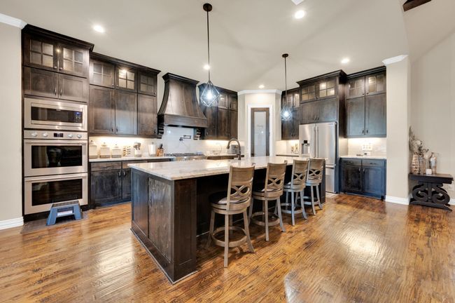 Kitchen with stainless steel appliances, decorative backsplash, dark brown cabinetry, a breakfast bar, and custom range hood | Image 10