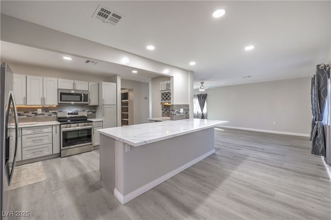 Kitchen with baseboards, visible vents, appliances with stainless steel finishes, light wood-type flooring, and backsplash | Image 12