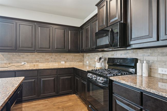 Kitchen featuring black appliances, light stone countertops, tasteful backsplash, and light wood-style floors | Image 12