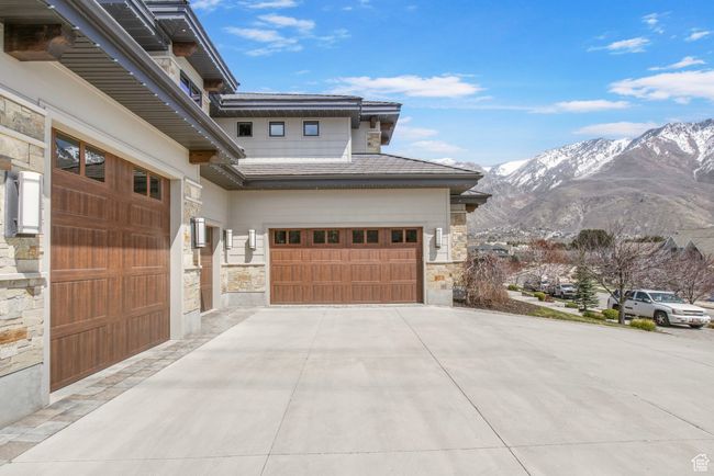 View of side of property featuring a mountain view, driveway, stone siding, an attached garage, and a tile roof | Image 122