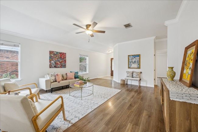 View of the living room from the kitchen area featuring vinyl wood flooring, ceiling fan, and windows allowing natural light | Image 4