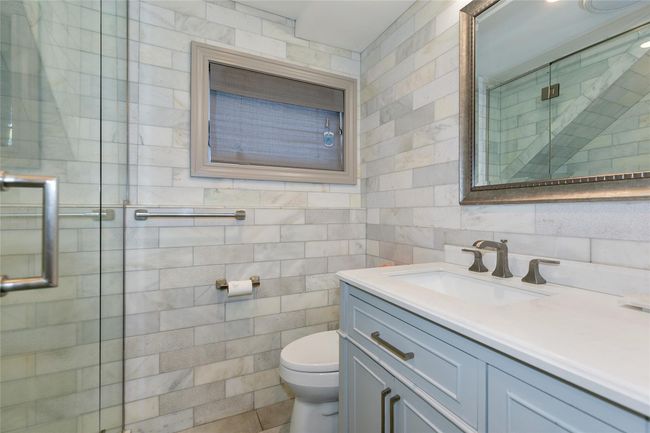 Bathroom featuring toilet, a stall shower, tile walls, and vanity | Image 12