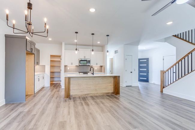 Kitchen featuring stainless steel microwave, light wood-type flooring, light countertops, tasteful backsplash, and a sink | Image 7