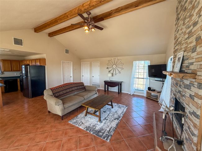Tiled living room with a ceiling fan, beamed ceiling, a fireplace, and visible vents | Image 11