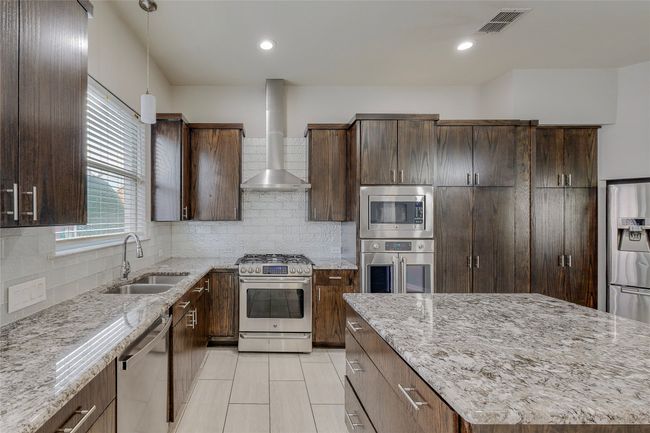 Kitchen featuring stainless steel appliances, a sink, wall chimney exhaust hood, light stone countertops, and recessed lighting | Image 18