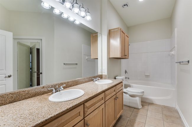 The primary en-suite bath exudes timeless style with natural-toned shaker cabinetry, dual sinks set in a polished granite countertop, and a shower/tub combination wrapped in elegant ceramic tile—offering both functionality and spa-like comfort. | Image 31