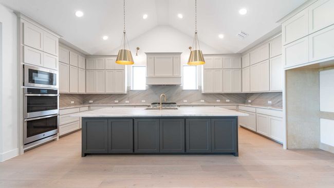 Kitchen with vaulted ceiling, stainless steel appliances, decorative backsplash, and a center island with sink | Image 11