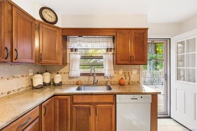 Kitchen with tasteful backsplash, light stone counters, light tile patterned floors, white dishwasher, and sink | Image 2