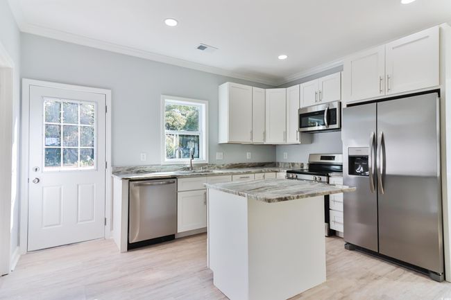 Kitchen featuring a kitchen island, light stone counters, sink, white cabinetry, and appliances with stainless steel finishes | Image 6