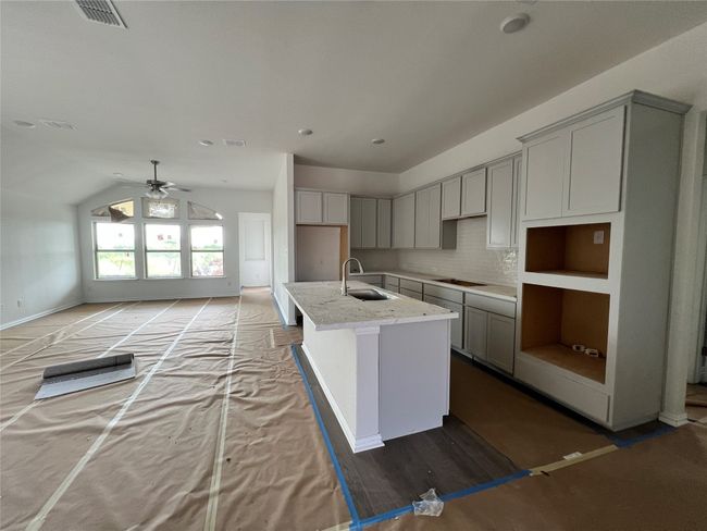 Kitchen with gray cabinetry, an island with sink, ceiling fan, decorative backsplash, and lofted ceiling | Image 4