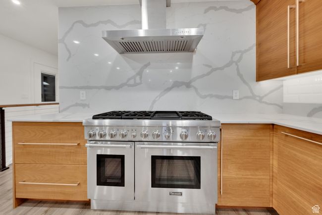 Kitchen featuring double oven range, wall chimney range hood, light stone counters, and modern cabinets | Image 7