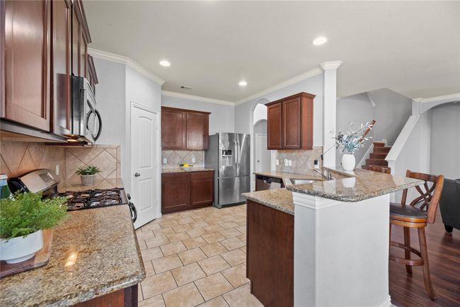 Beautifully designed, the kitchen features stainless steel appliances, dark wood cabinetry, tile backsplash, and a pantry. Cooking not only becomes fun in this space; it becomes fashionable and Instagram-ready! | Image 5