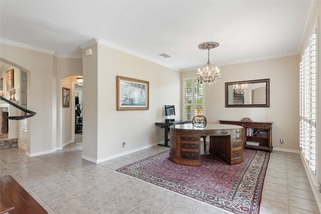 Spacious home office with elegant chandelier and natural light through plantation shutters. | Image 8