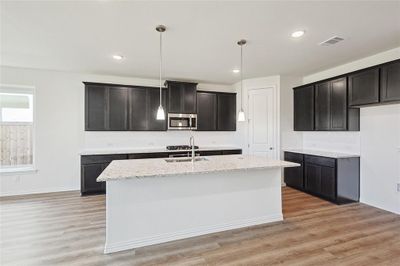 Kitchen with a center island with sink, light hardwood / wood-style flooring, light stone counters, and decorative light fixtures | Image 3