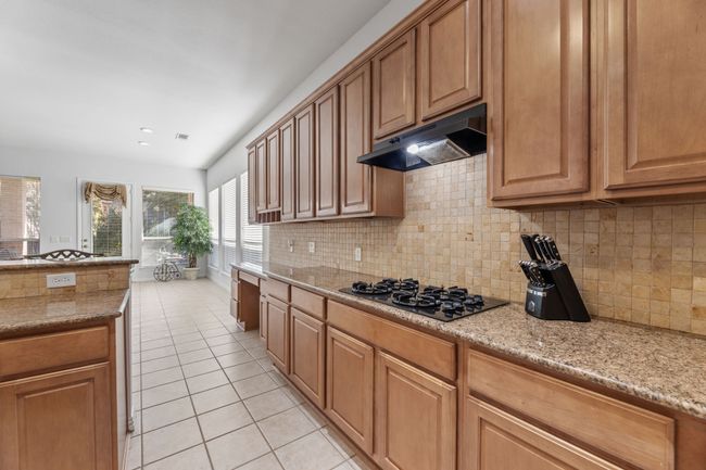 Kitchen featuring light stone counters, light tile patterned floors, backsplash, and black gas stovetop | Image 19