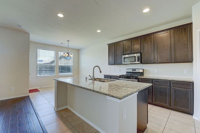 Kitchen featuring a sink, appliances with stainless steel finishes, a kitchen island with sink, light stone counters, and tasteful backsplash | Image 6