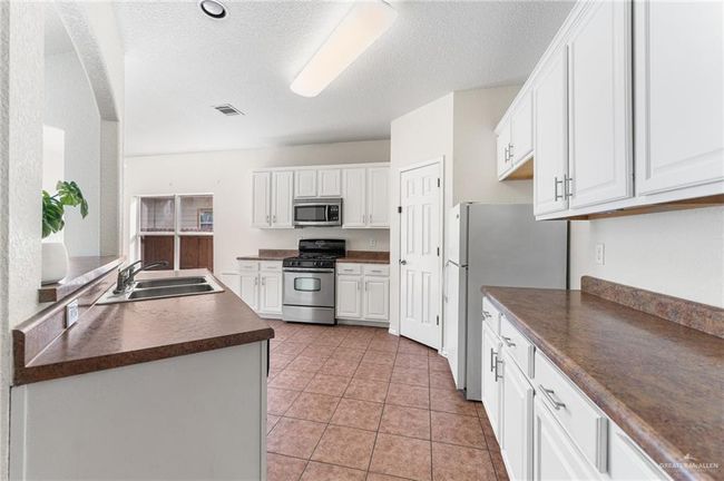 Kitchen with appliances with stainless steel finishes, dark countertops, white cabinets, a textured ceiling, and light tile patterned floors | Image 22
