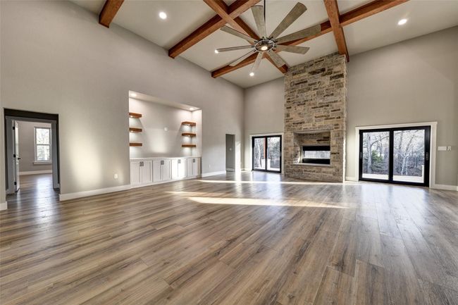 Unfurnished living room with a stone fireplace, ceiling fan, hardwood / wood-style floors, and a towering ceiling | Image 14