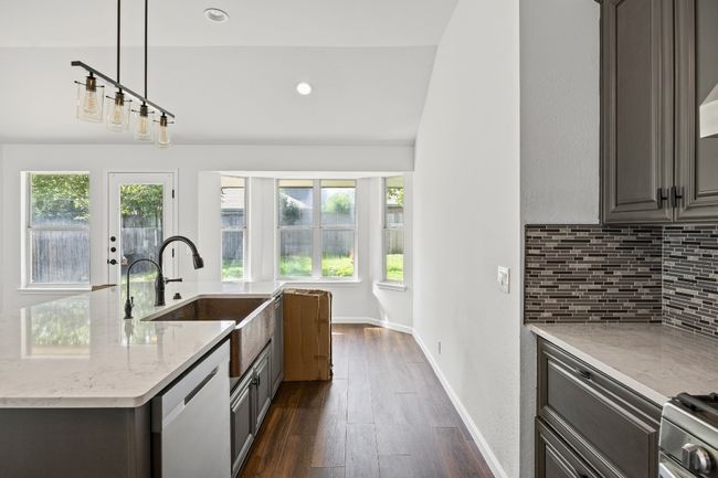 Kitchen with decorative backsplash, dishwasher, light stone counters, dark wood-type flooring, and a kitchen island with sink | Image 9
