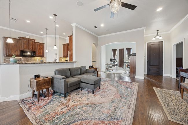 Living area featuring arched walkways, ceiling fan, dark wood-type flooring, crown molding, and recessed lighting | Image 6