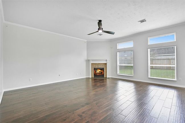 The spacious family room is anchored by a cozy gas fireplace with a classic milled wood mantle, flanked by tall windows that bathe the space in natural light. | Image 9