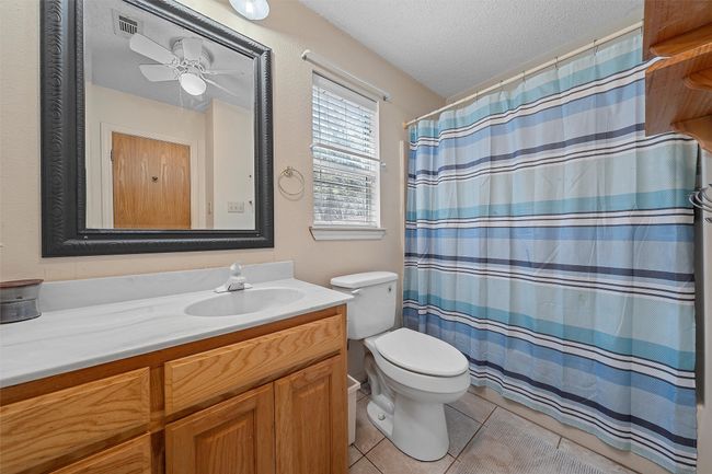 Bathroom with a textured ceiling, toilet, curtained shower, tile patterned flooring, and vanity | Image 23