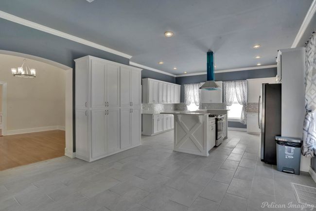 Kitchen with decorative backsplash, white cabinetry, appliances with stainless steel finishes, island range hood, and crown molding | Image 4