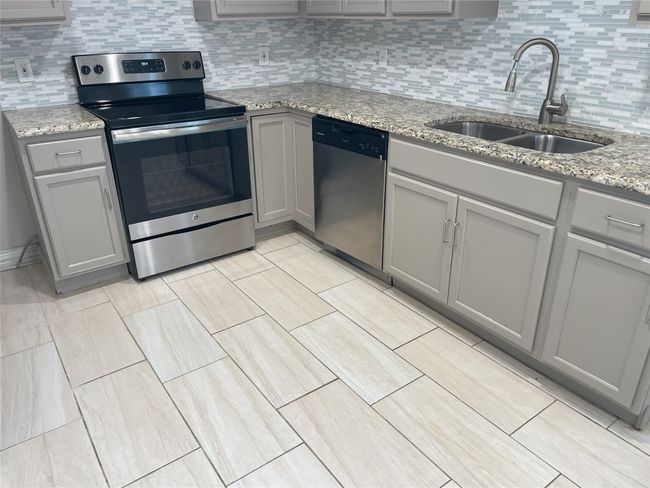 Kitchen with gray cabinets, appliances with stainless steel finishes, decorative backsplash, and light stone countertops | Image 9