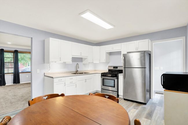 kitchen with stainless steel appliances, a sink, white cabinetry, light countertops, and light wood finished floors | Image 7