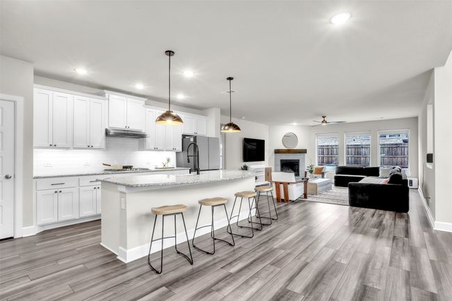 Kitchen featuring an island with sink, stainless steel appliances, white cabinets, under cabinet range hood, and open floor plan | Image 7