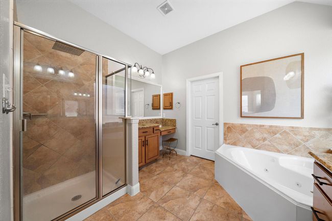 The primary bath features dual vanities, a soaking tub, and a glass-enclosed shower, offering both luxury and functionality. Tile flooring and elegant finishes create a serene environment for relaxation. | Image 30