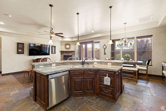 Kitchen featuring stainless steel dishwasher, stone tile flooring, a tray ceiling, a fireplace, and a ceiling fan | Image 31