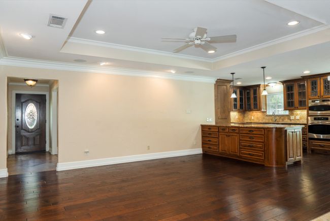 Kitchen with brown cabinets, dark wood-style floors, ceiling fan, decorative backsplash, and glass insert cabinets | Image 10