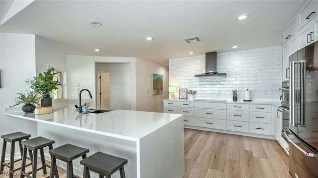 Kitchen with wall chimney range hood, light stone counters, decorative backsplash, high end refrigerator, and a breakfast bar | Image 15