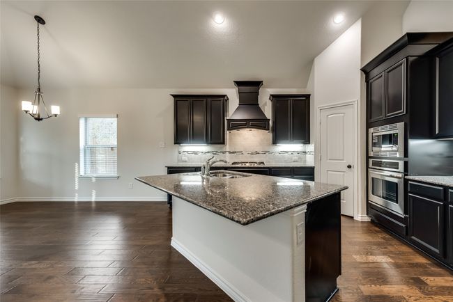 Kitchen featuring appliances with stainless steel finishes, custom range hood, dark stone counters, an island with sink, and dark wood-type flooring | Image 7