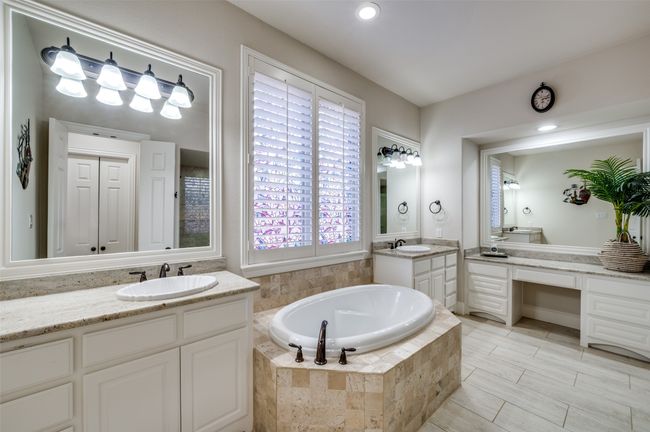 The spa-like ensuite primary bath offers an abundance of cabinetry for all your storage needs, along with double vanities and a dedicated makeup area. Framed mirrors, granite countertops, and upgraded tile add a sophisticated touch to this elegant space. | Image 21