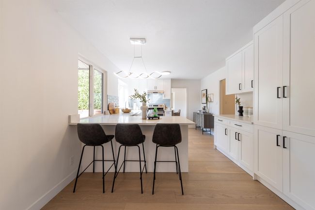 Kitchen featuring backsplash, white cabinetry, a kitchen breakfast bar, a peninsula, and light wood-style floors | Image 14