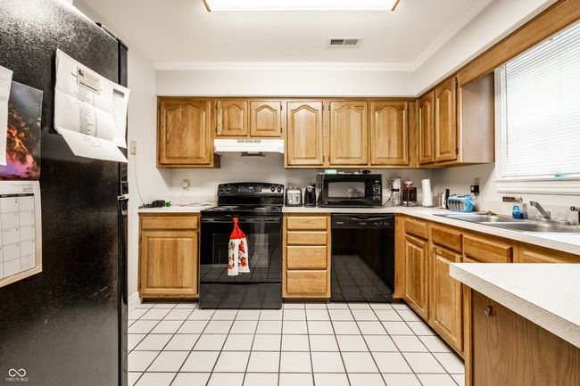kitchen featuring a sink, visible vents, crown molding, under cabinet range hood, and black appliances | Image 12