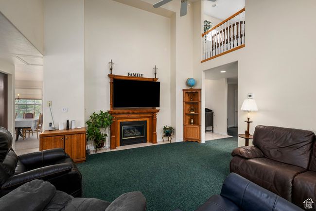 Carpeted living area featuring baseboards, a high ceiling, a fireplace with flush hearth, and ceiling fan | Image 14