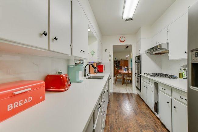 Kitchen with under cabinet range hood, light countertops, a sink, white cabinetry, and appliances with stainless steel finishes | Image 9
