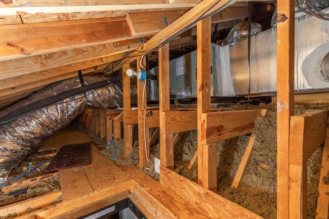 This photo shows a well-maintained attic space with visible insulation, wooden framing, and ductwork and recently installed HVAC unit. | Image 49