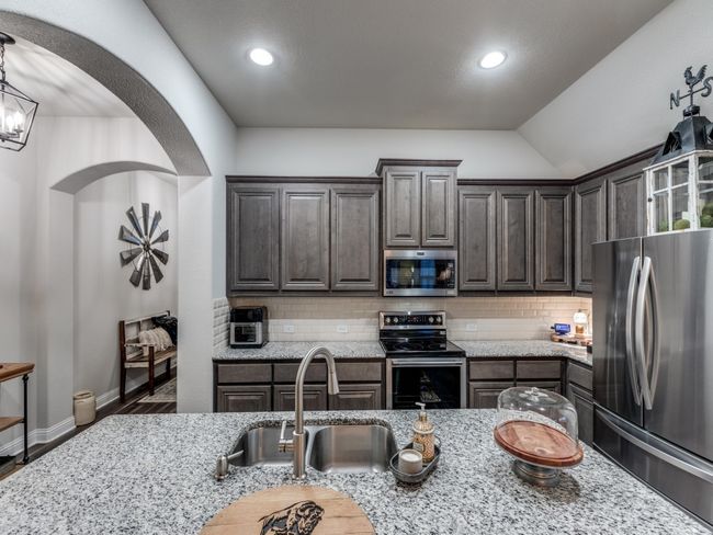 Kitchen featuring tasteful backsplash, sink, dark brown cabinetry, stainless steel appliances, and light stone countertops | Image 14