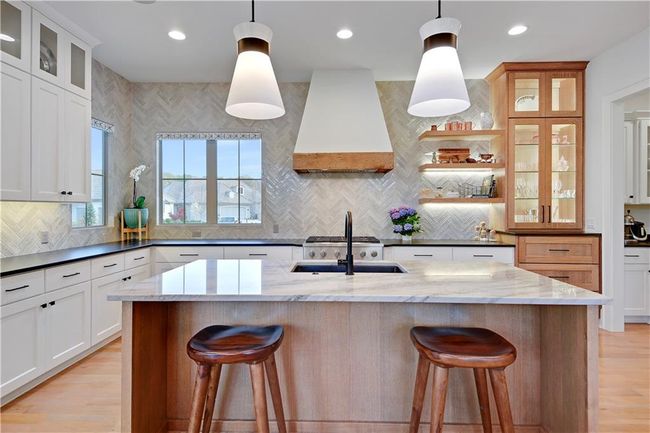 Kitchen with backsplash, custom exhaust hood, a sink, and a breakfast bar | Image 18