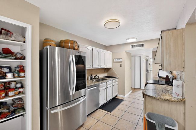 Kitchen featuring stainless steel appliances, a sink, decorative backsplash, light tile patterned floors, and white cabinetry | Image 9